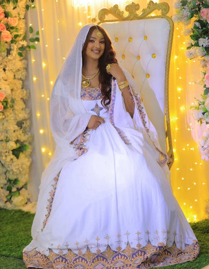 Woman in a white and gold traditional Habesha Dress sitting on an ornate chair with floral decorations and string lights in the background.