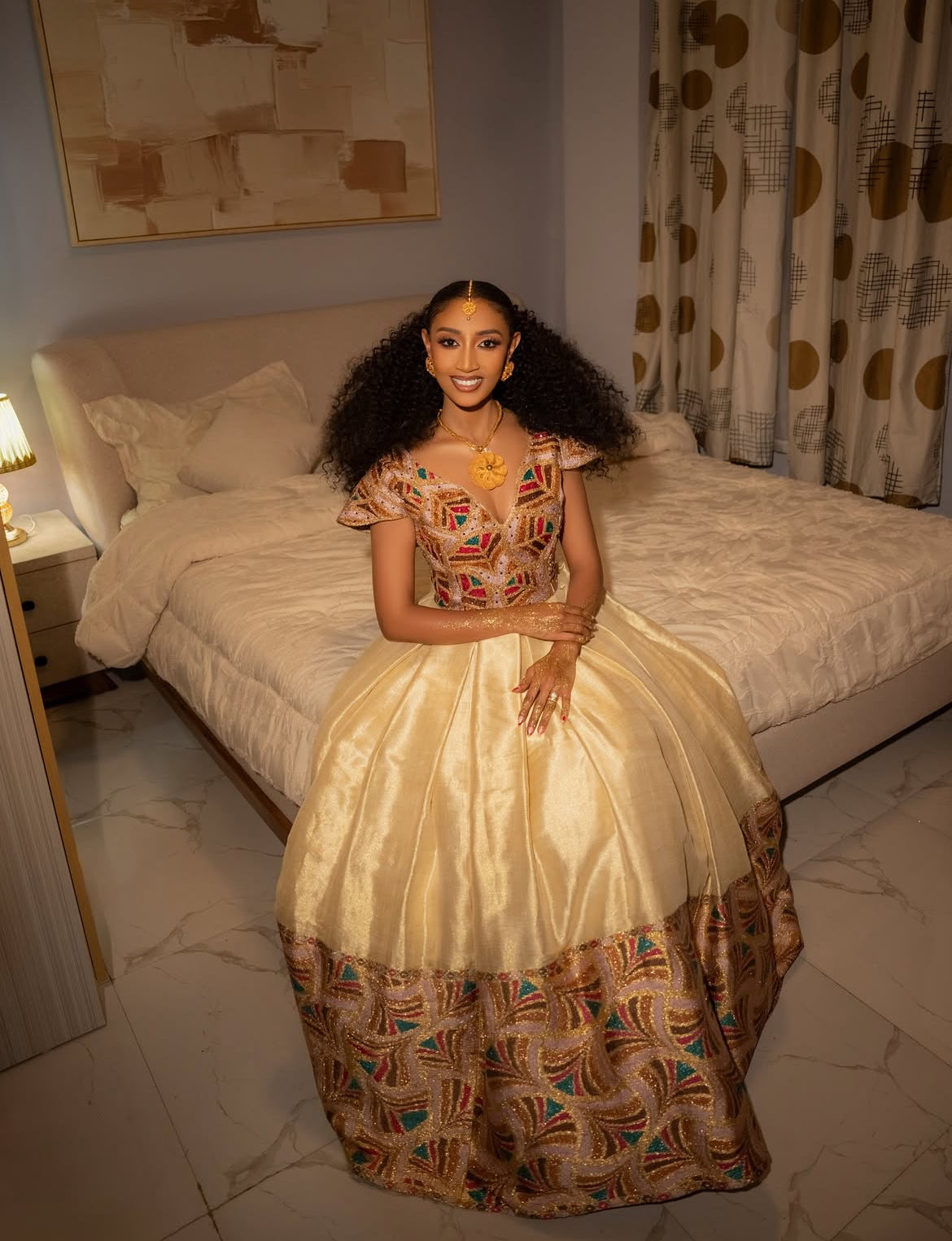 Woman in a patterned Habesha wedding Dress sitting on a bed in a bedroom.