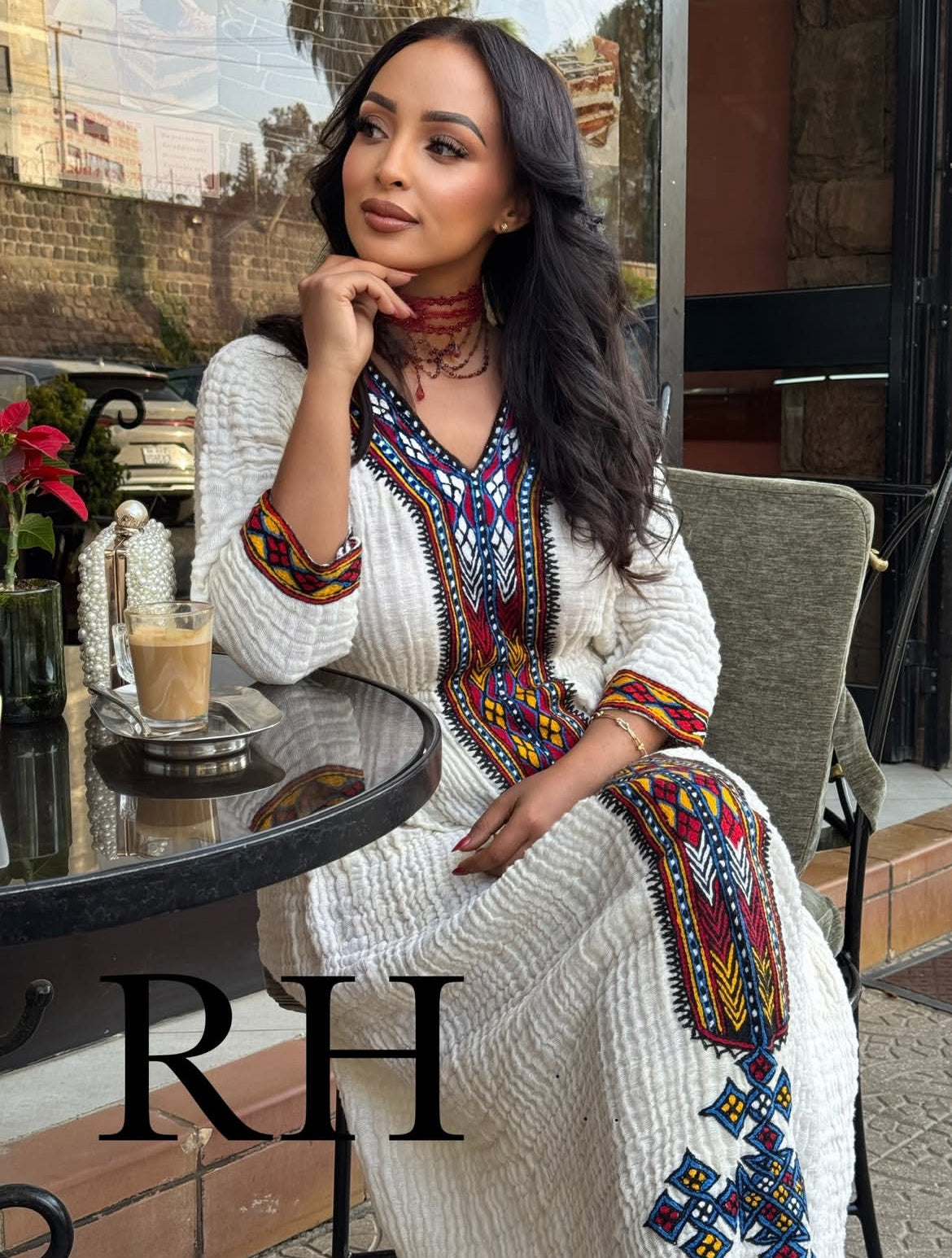 Woman in a colorful Traditional Ethiopian Dress sitting at an outdoor cafe with 'RH' branding.