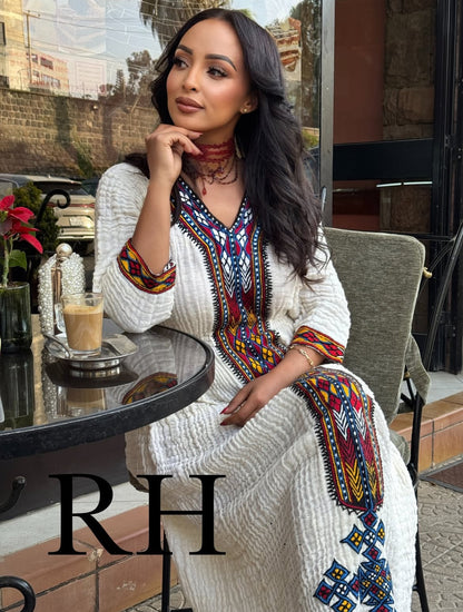 Woman in a colorful Traditional Ethiopian Dress sitting at an outdoor cafe with 'RH' branding.