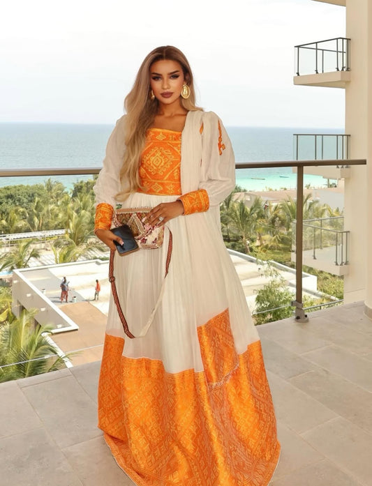 Woman in a white and orange traditional habesha  kemis standing on a balcony with ocean view