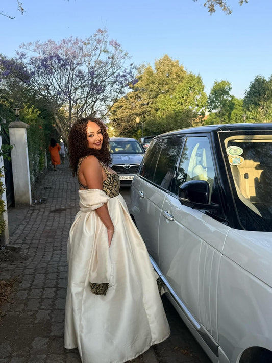 Woman in a white Ethiopian Dress standing next to a white car on a sunny day.