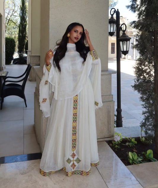 Woman in a white traditional Habesha Zuria with gold embroidery standing outdoors.