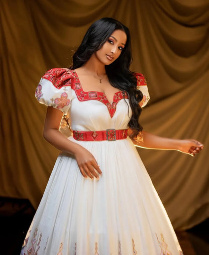 Woman in a white Habesha Wedding Dress with red accents against a brown curtain background