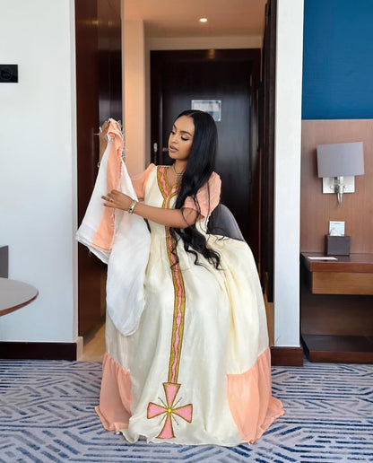 Woman holding a traditional Ethiopian Dress in a room with a blue wall and wooden furniture.