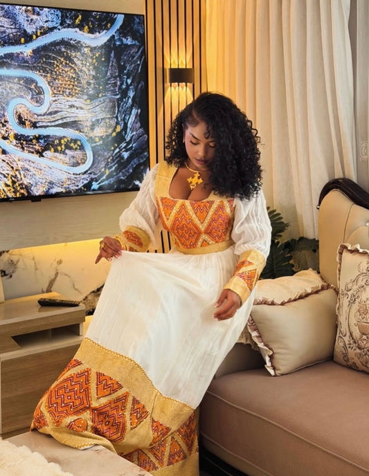 Woman in traditional attire sitting on a couch in a living room with a TV in the background.