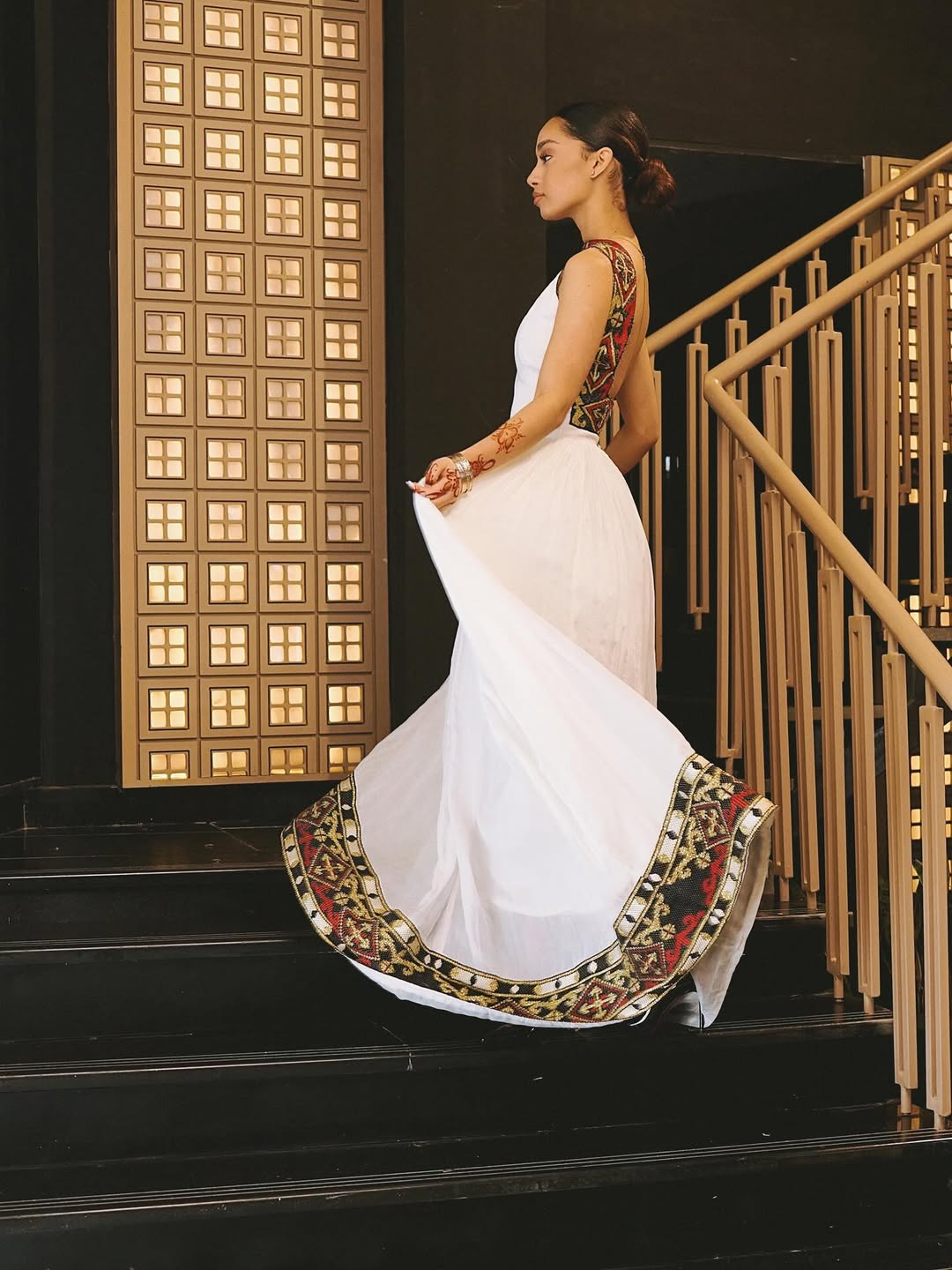Habesha Woman in a white habesha dress with a colorful border walking up a staircase.
