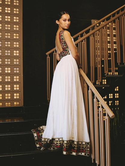 Woman in a white ethiopian dress with patterned top standing on a staircase at night.