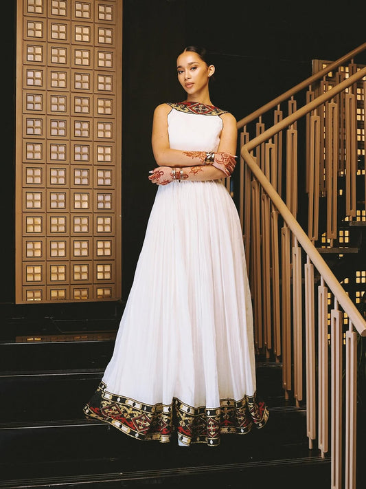 Woman in a white traditional ethiopian dress with intricate patterns standing on a staircase.