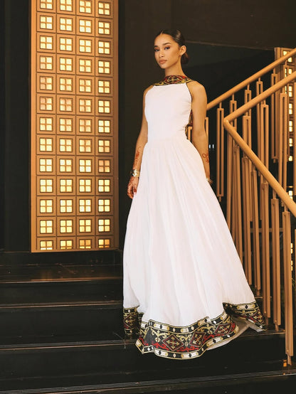 Woman in a white habesha dress with decorative elements standing on a staircase.