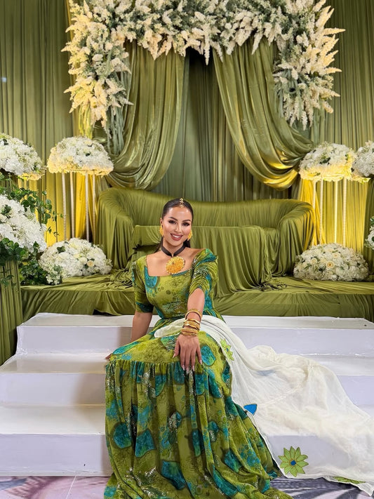 Woman in a green Shiffon Habesha
 sitting on a decorated stage with floral arrangements and green curtains.