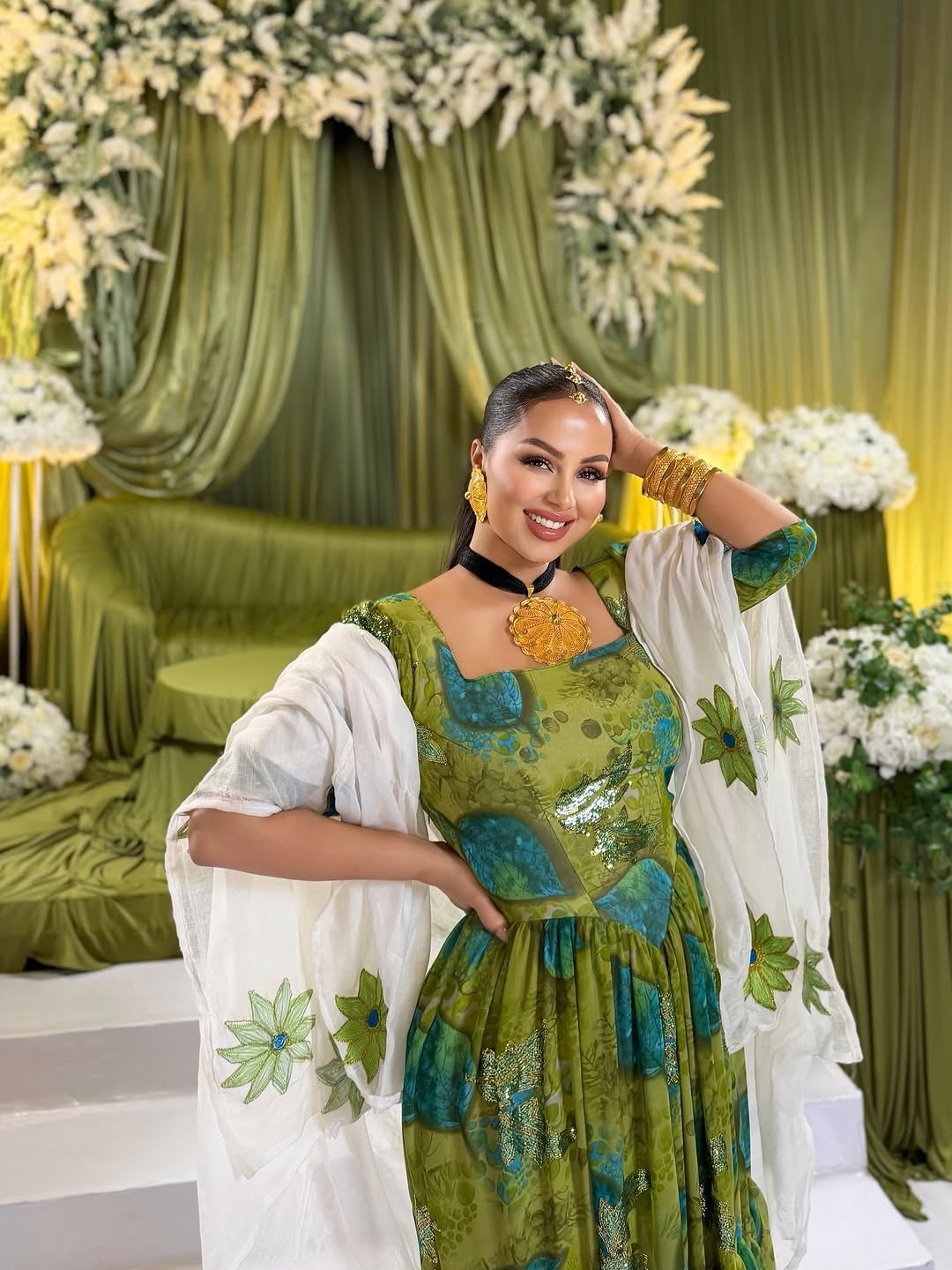 Woman in a green and white traditional habesha shiffion posing in front of floral decorations