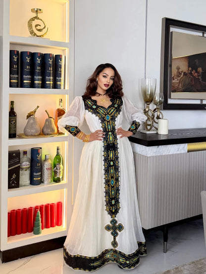 Woman in a white and black embroidered dress standing in a modern interior setting.