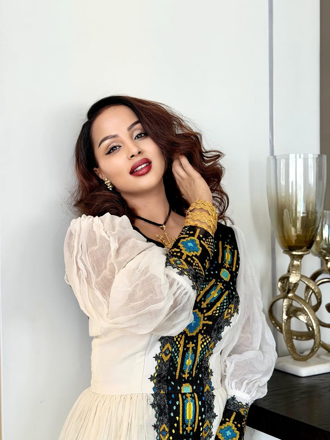 Woman wearing a white blouse with black and blue patterned sleeves against a white wall.