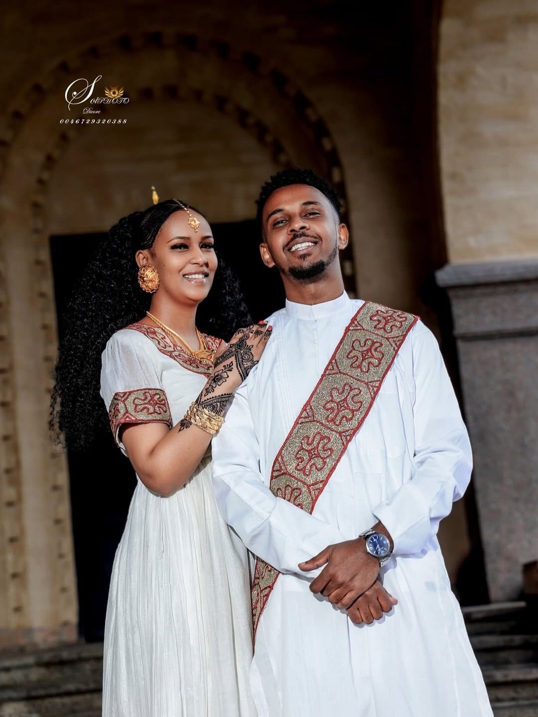 Couple in traditional Red Matching Habesha Set  standing together in front of an architectural background