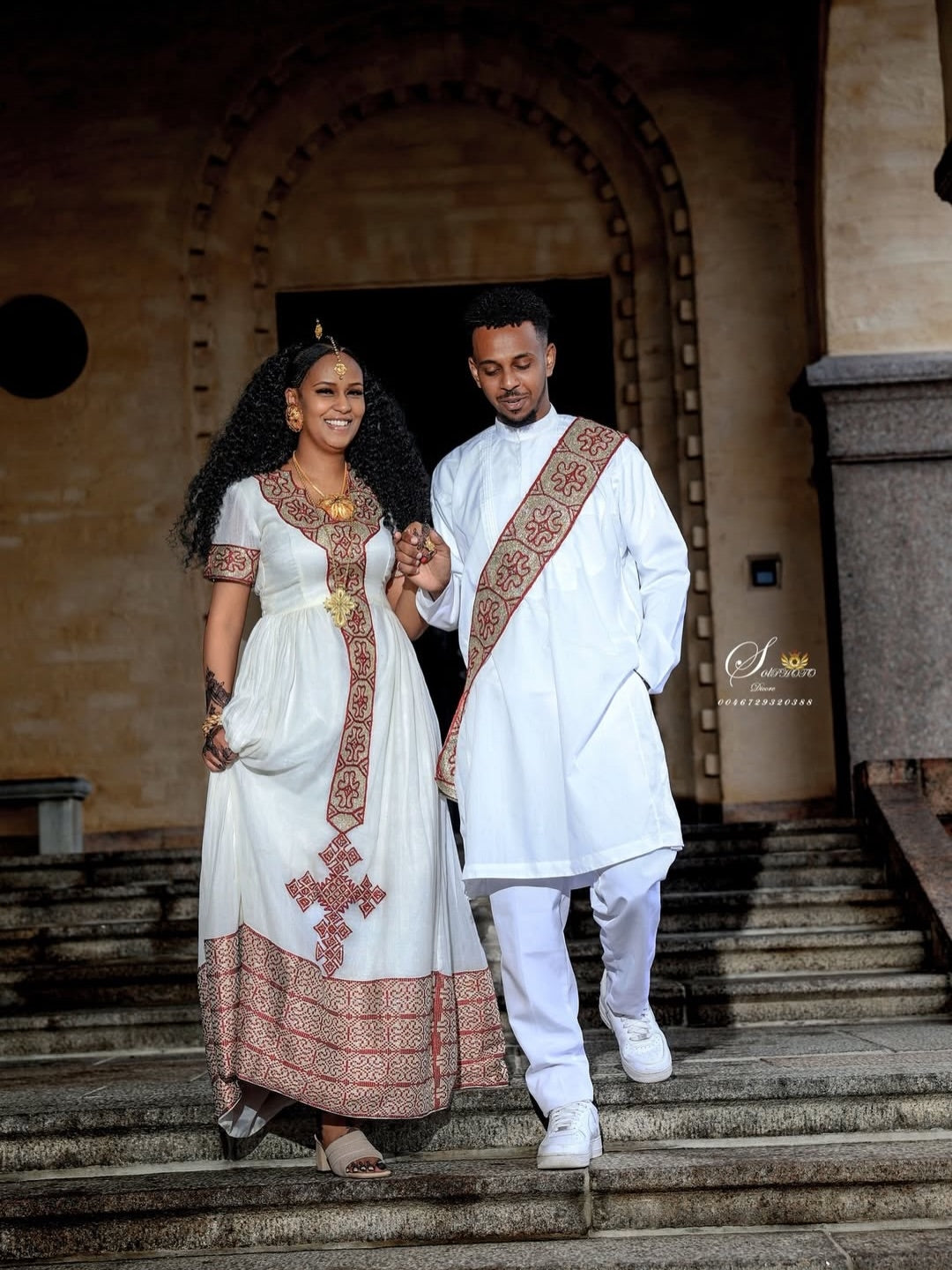 Couple in traditional Red Matching Habesha Set  walking down steps in front of an archway.