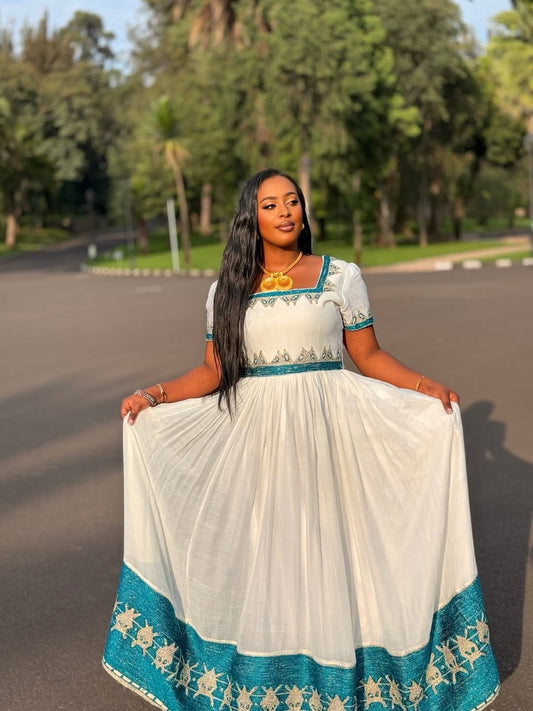 A woman wearing a white habesha kemis with teal and gold embroidery, holding out the skirt to show its full flow in an outdoor park setting.