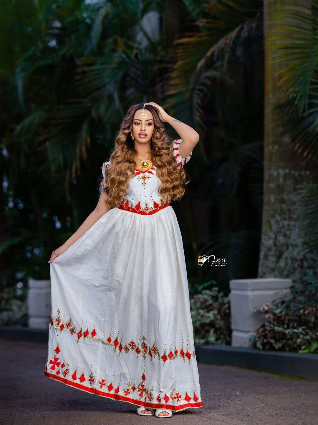 Woman in a white and red traditional outfit with floral patterns, standing outdoors.