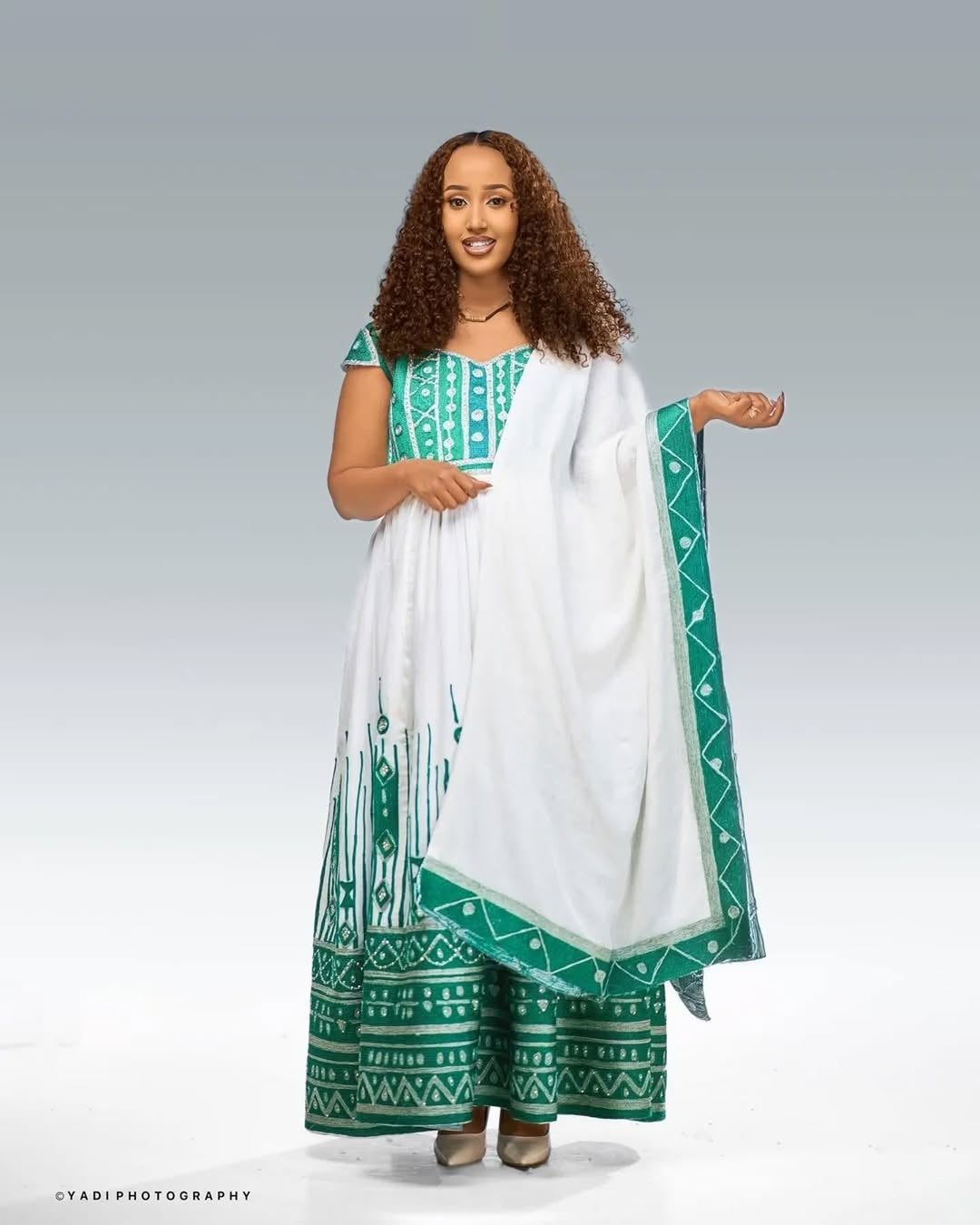 Woman wearing a green and white Ethiopian Wedding Dress  with a white scarf against a gray background