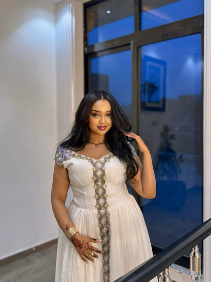 Woman in a white Ethiopian Traditional Dress with decorative elements standing indoors.