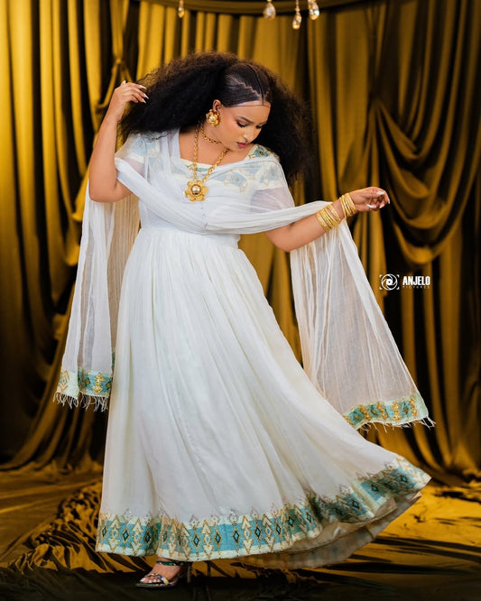 Woman in a white traditional Green Ethiopian Dress with gold and green details against a yellow curtain background