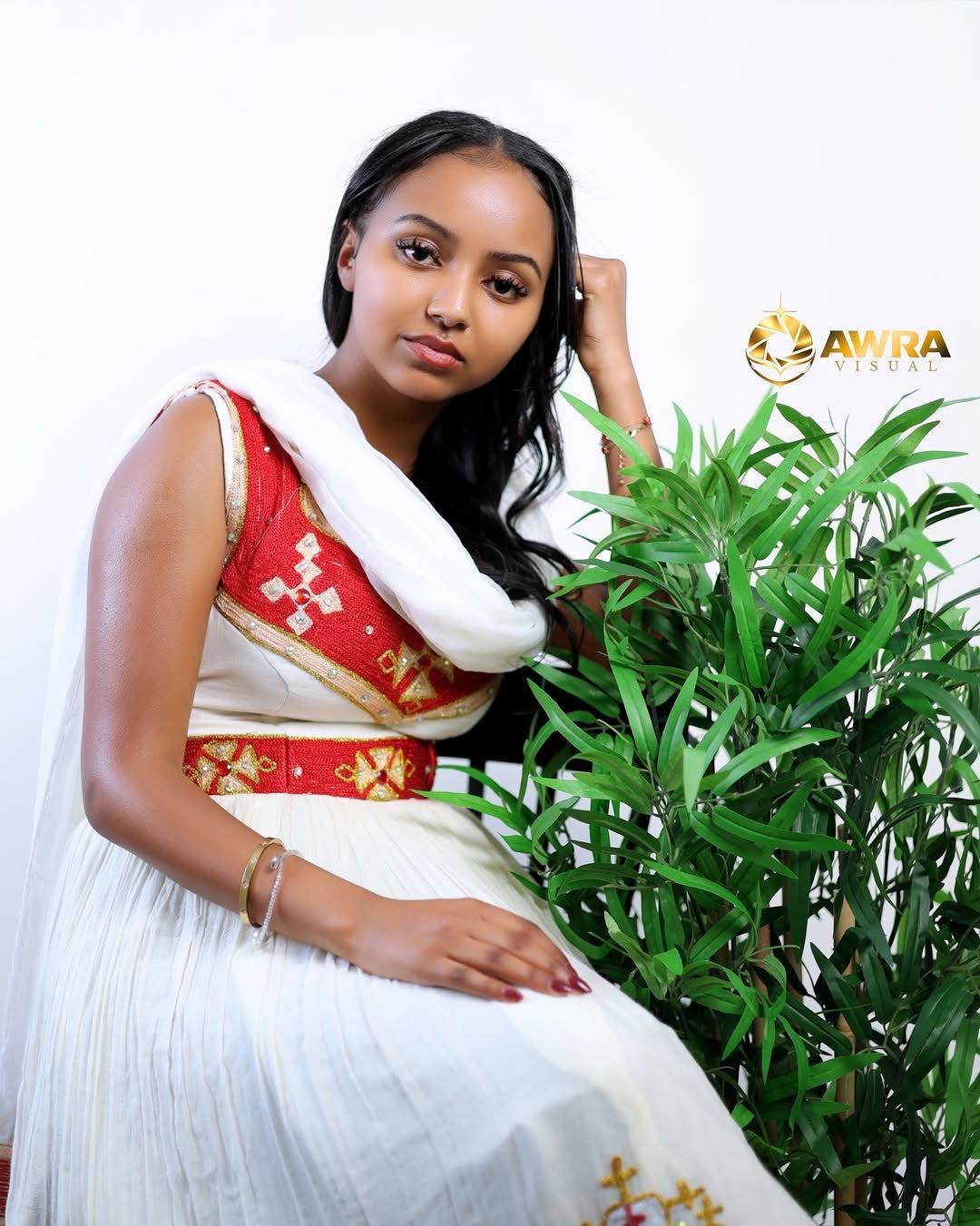 Woman in a traditional Red Habesha Libs  with a plant in the background, featuring the AWRA logo.