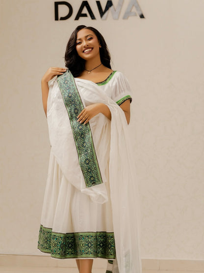 Woman wearing a white saree with green border, holding the saree, against a plain background with 'DAWA' branding.