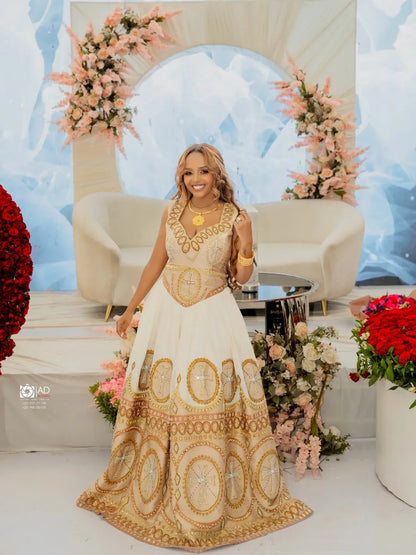 Woman in a gold and white Habesha Libs standing in a decorated room with flowers and a blue abstract wall.
