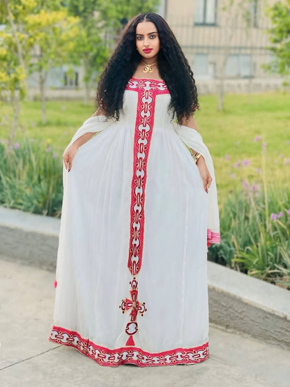 Woman wearing a white Habesha Zuria with red embroidery in an outdoor setting