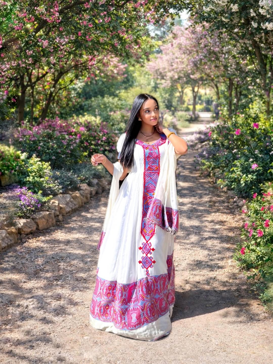 Woman in a habesha dress standing in a garden with pink flowers