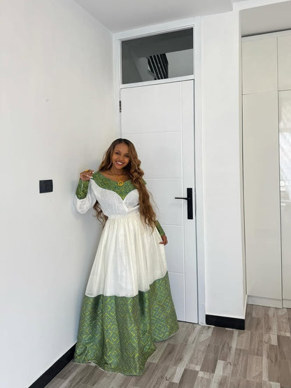 Woman in a green and white dress standing in a room with white walls and a door.