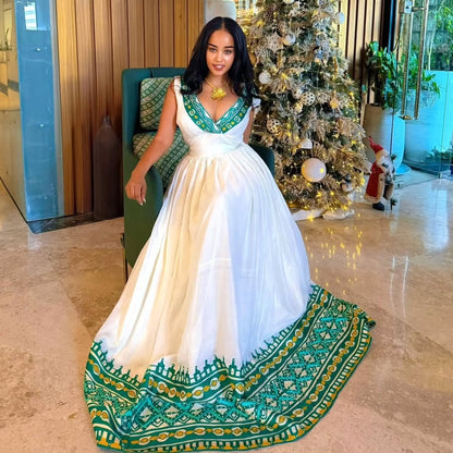 Woman in a white and green  Habesha Kemis  standing in a decorated room with a Christmas tree.