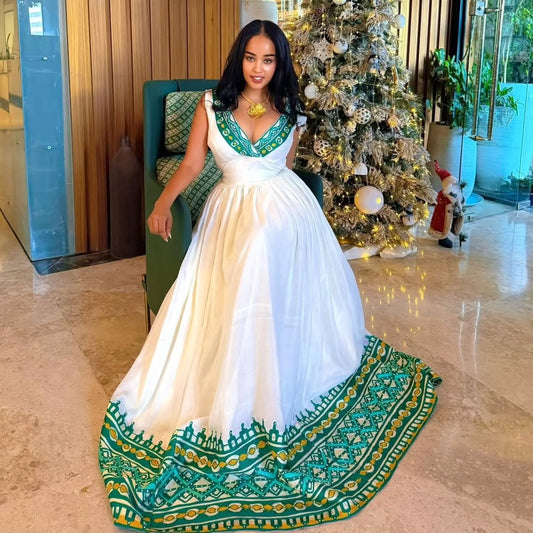 Woman in a white and green  Habesha Kemis  standing in a decorated room with a Christmas tree.