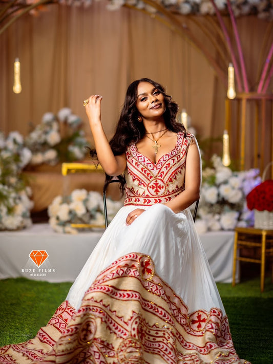 Woman in a red and white Ethiopian Traditional Dress embroidered red Ethiopian traditional dress sitting in an elegant indoor setting with floral decorations.