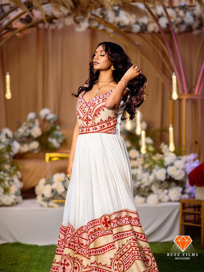 Woman in a white and red red Ethiopian traditional dress standing in a decorated indoor setting with floral arrangements and candles.