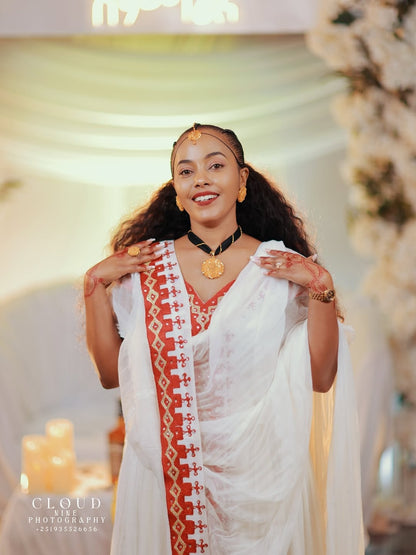 Woman in a white Traditional Dress with  red and gold border, posing indoors with decorative background.