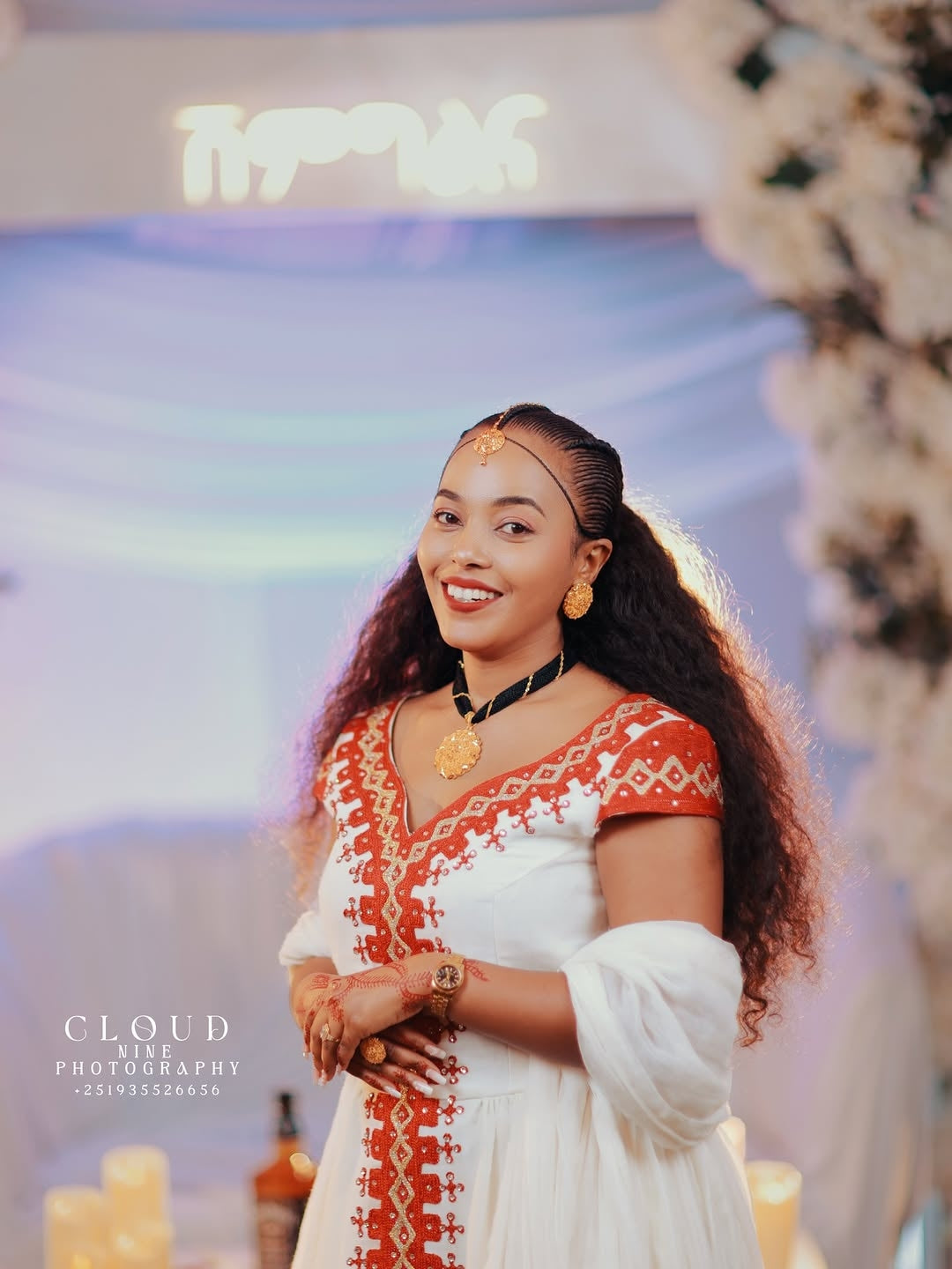 Woman in a white Traditional Dress with red embroidery standing in front of a colorful background