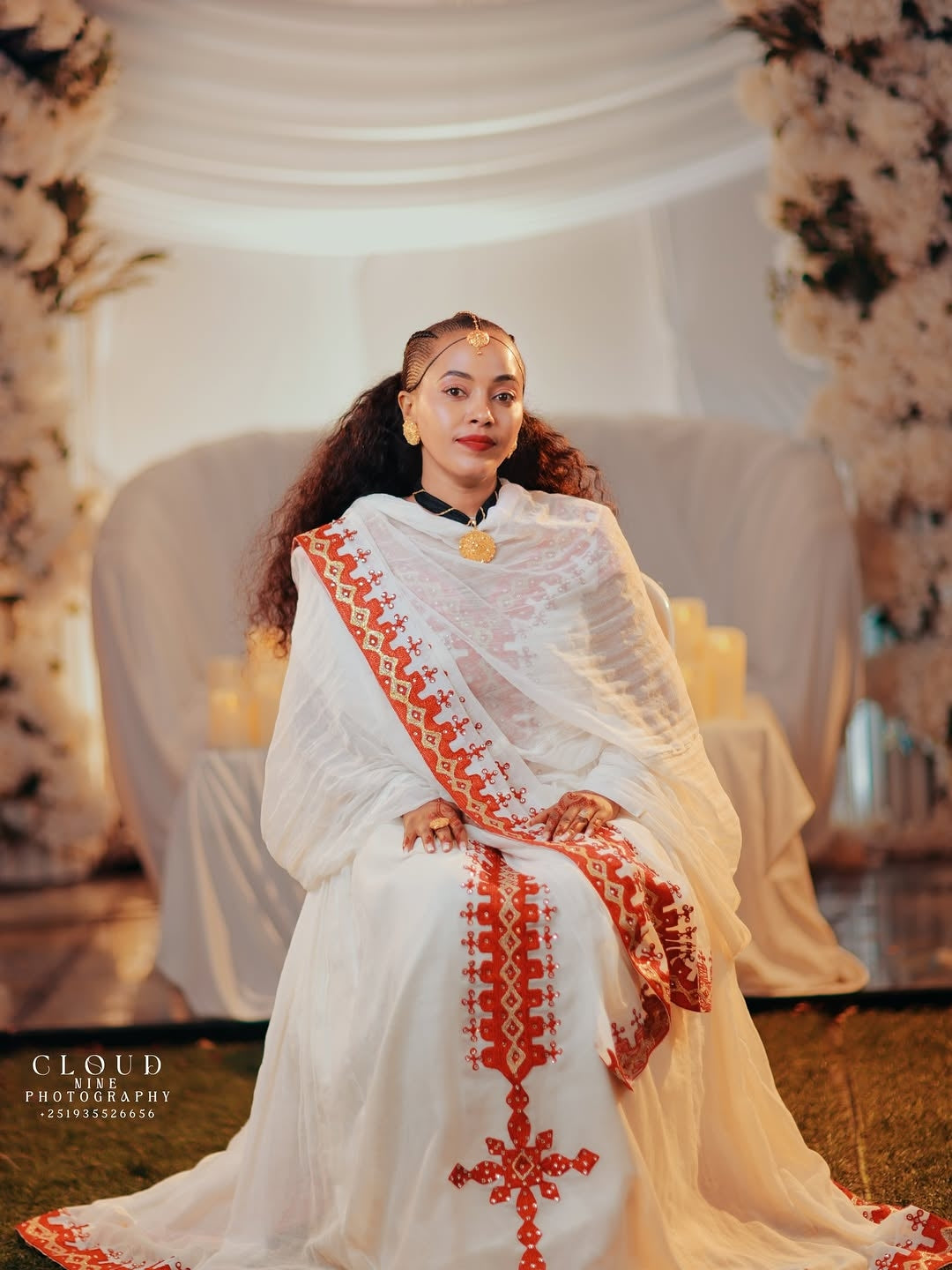 Woman in a white and red Traditional Dress sitting in a decorated indoor setting.