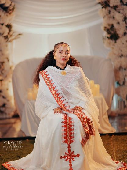 Woman in a white and red Traditional Dress sitting in a decorated indoor setting.