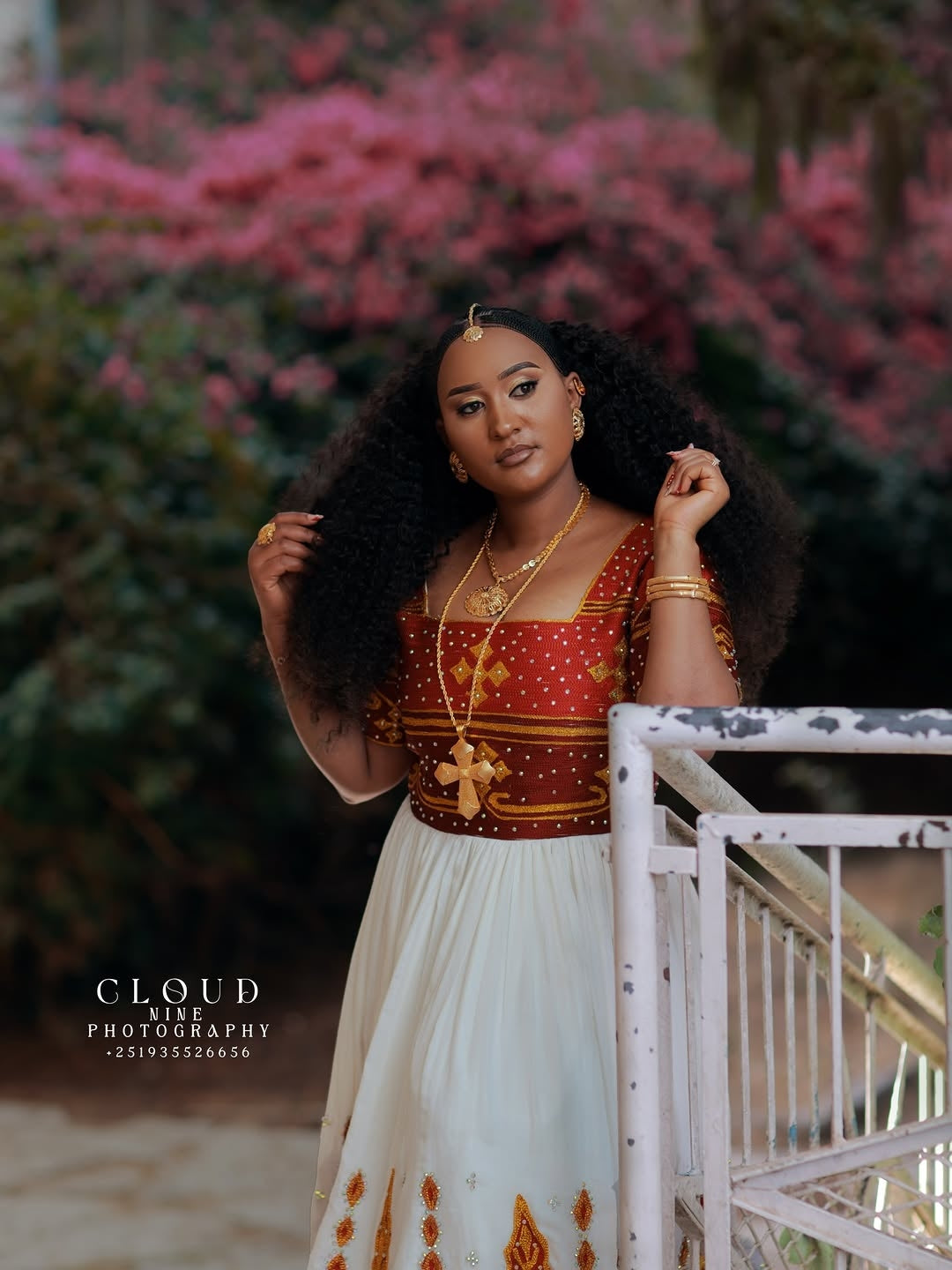 Woman in a traditional Red and White Habesha Matching Couple Set standing outdoors with blurred pink flowers in the background