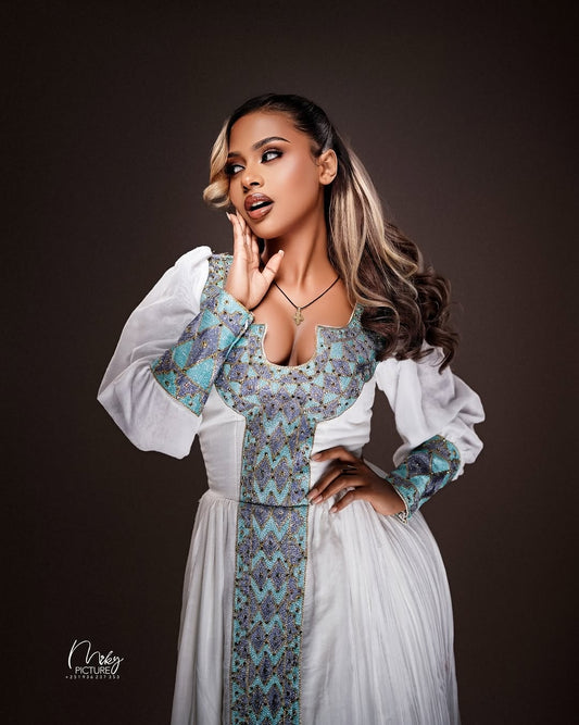 Woman wearing a patterned Habesha Zuria with a white jacket against a dark background