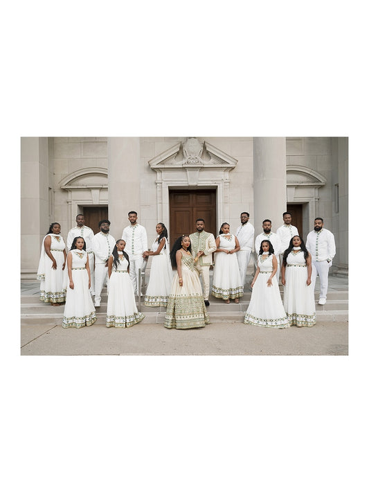A group of people posing outdoors in front of a grand stone building with columns. The  Traditional matching couple set  is dressed in coordinated traditional formal wear, with several women in white and gold lehengas and several men in white kurta sets.