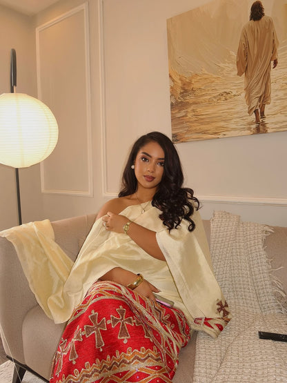 Woman in a white and red traditional outfit sitting on a couch in a room with a painting on the wall.