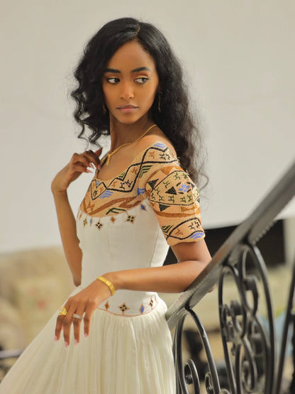 Woman wearing a patterned top and white Gold Habesha Libs leaning against a railing.