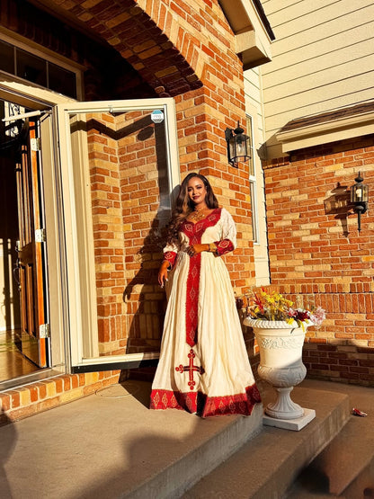 Woman in a white and red Ethiopian Libs standing on a porch with a brick wall background