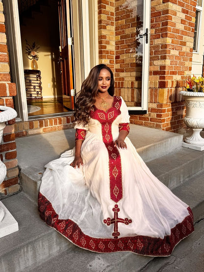 Woman in a white and red Ethiopian Libs sitting on steps outside a brick building.