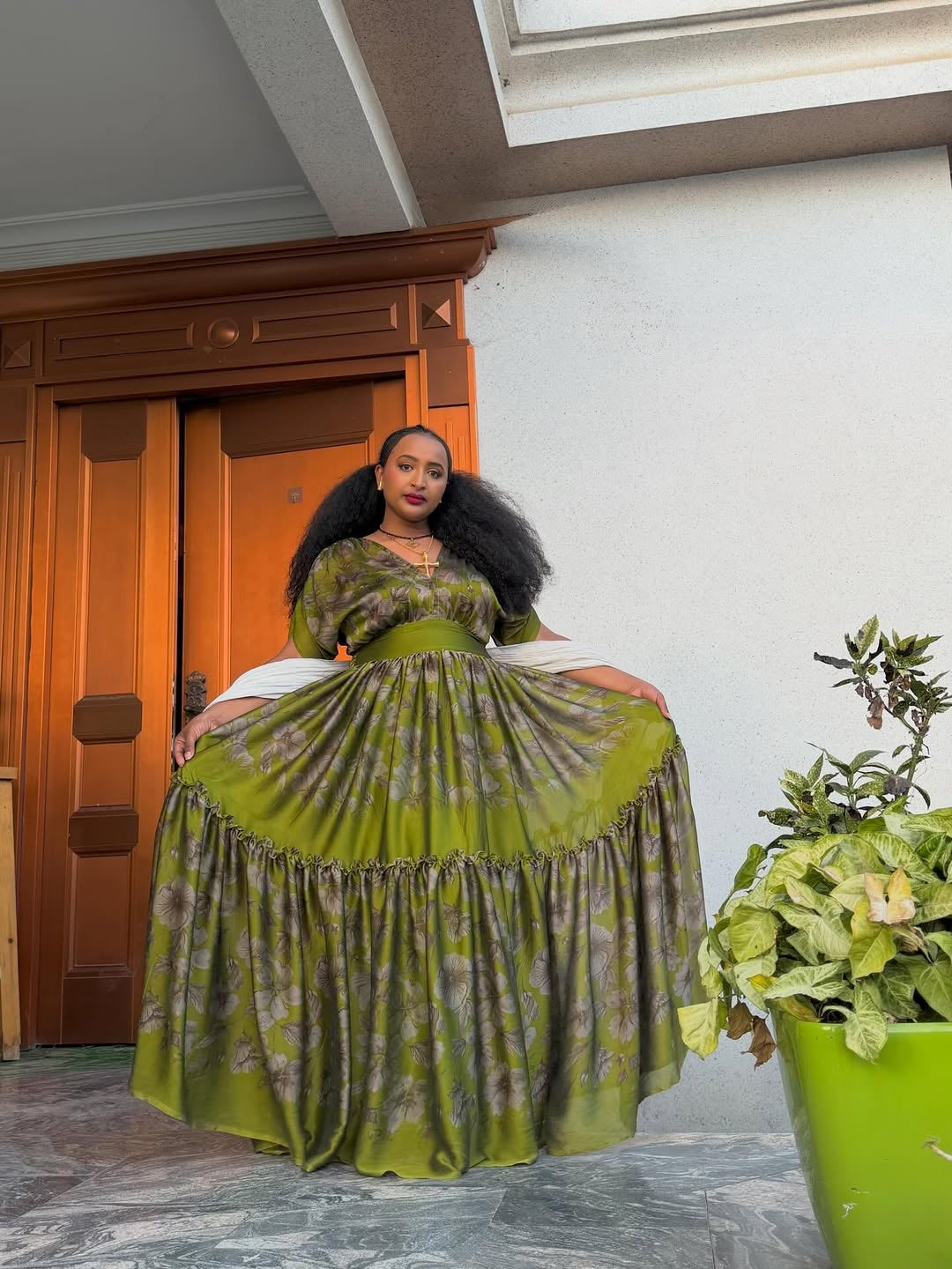 Woman in a green dress standing in a room with a wooden door and potted plant.