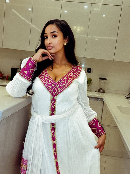 Woman in a white and pink Ethiopian Dress standing in a kitchen.