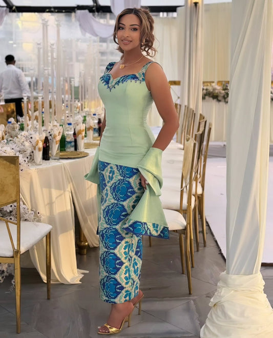 Woman wearing a light green Ethiopian Dress with blue patterned embroidery and a matching shawl.