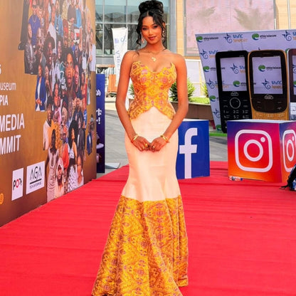 Woman posing in a strapless modern Habesha dress featuring a yellow woven patterned peplum bodice and a white skirt with a matching detailed yellow hem.